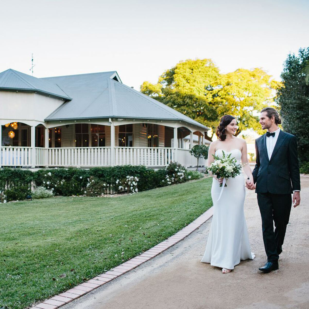 Bride and groom walking down a garden path with Bangalow Guesthouse in the background during a vintage-style wedding