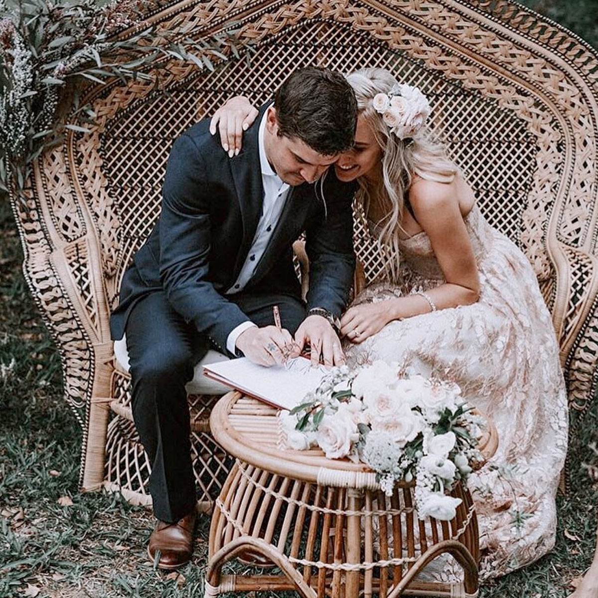 Bride and groom signing their marriage certificate on a vintage rattan loveseat at Bangalow Guesthouse